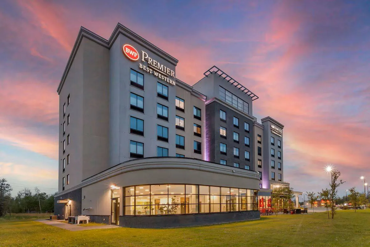Hotel building with "BWP Premier Best Western" sign at sunset, featuring large windows. Pink and orange sky adds warmth to the scene.