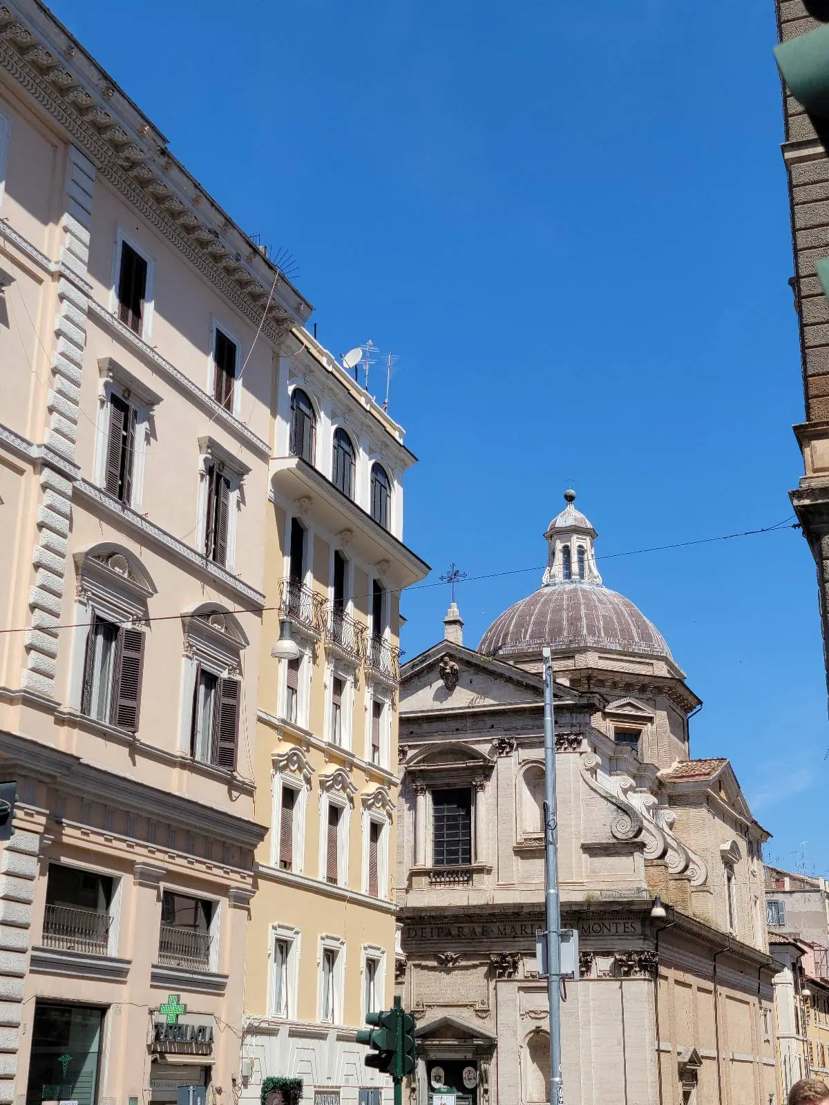 A city street with historic buildings and a domed church under a clear blue sky. The architecture features ornate details and large windows.