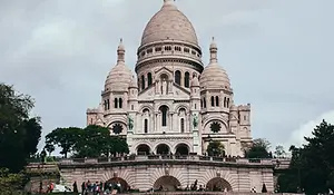 The white domes of the Sacrรฉ-Cลur Basilica in Paris rising above the hillside trees under a clear sky.