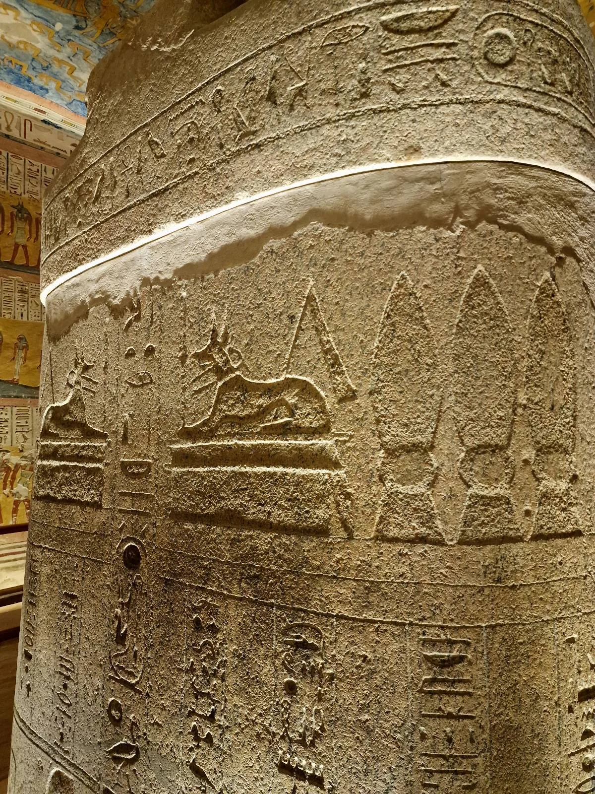 Ancient Egyptian stone pillar adorned with detailed hieroglyphics and carvings, including an image of a reclining animal, possibly an ox or similar creature, in an indoor setting.