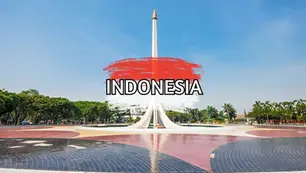 A tall white monument with a golden tip stands in a circular plaza surrounded by greenery under a clear blue sky. "INDONESIA" is written in bold letters over a red paint splash in the foreground.