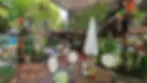Outdoor café with colorful flags, plants, and patrons sitting at tables. Warm, vibrant atmosphere with decorated, shaded setting.