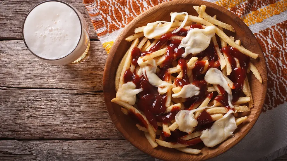 A wooden bowl of fries topped with melted cheese and a dark sauce. A frothy glass of beer is beside it, placed on a rustic wooden table with decorative cloth.