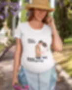 A pregnant woman wearing a white T-shirt with a Thanksgiving-themed design stands outdoors.