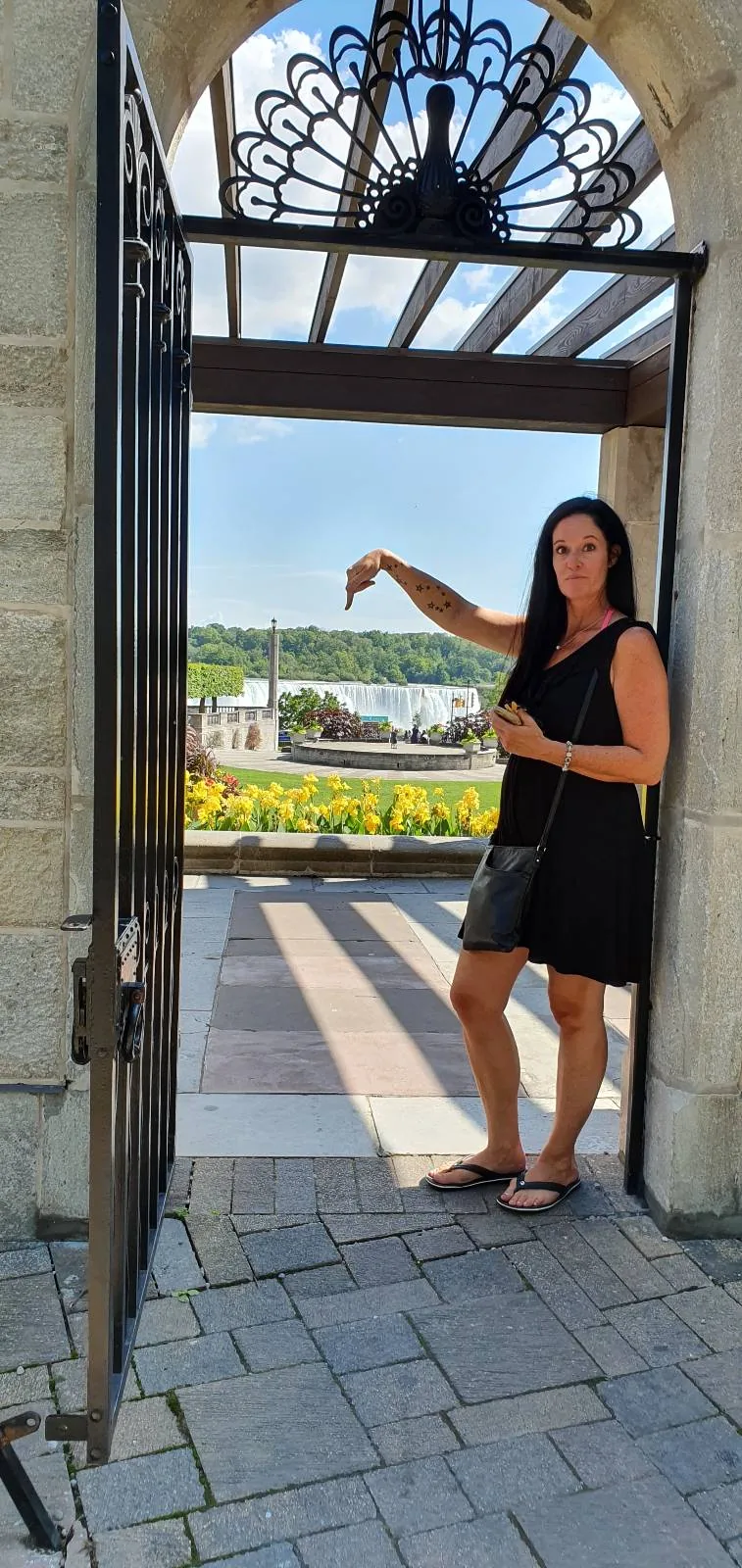 A woman standing at an open gate, pointing to something outside of the frame.