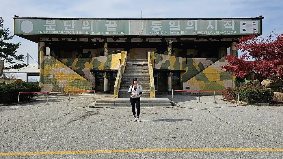 Woman in front of a camo-painted building with text "End of Separation, Beginning of Unification." Red tree and clear sky in background.