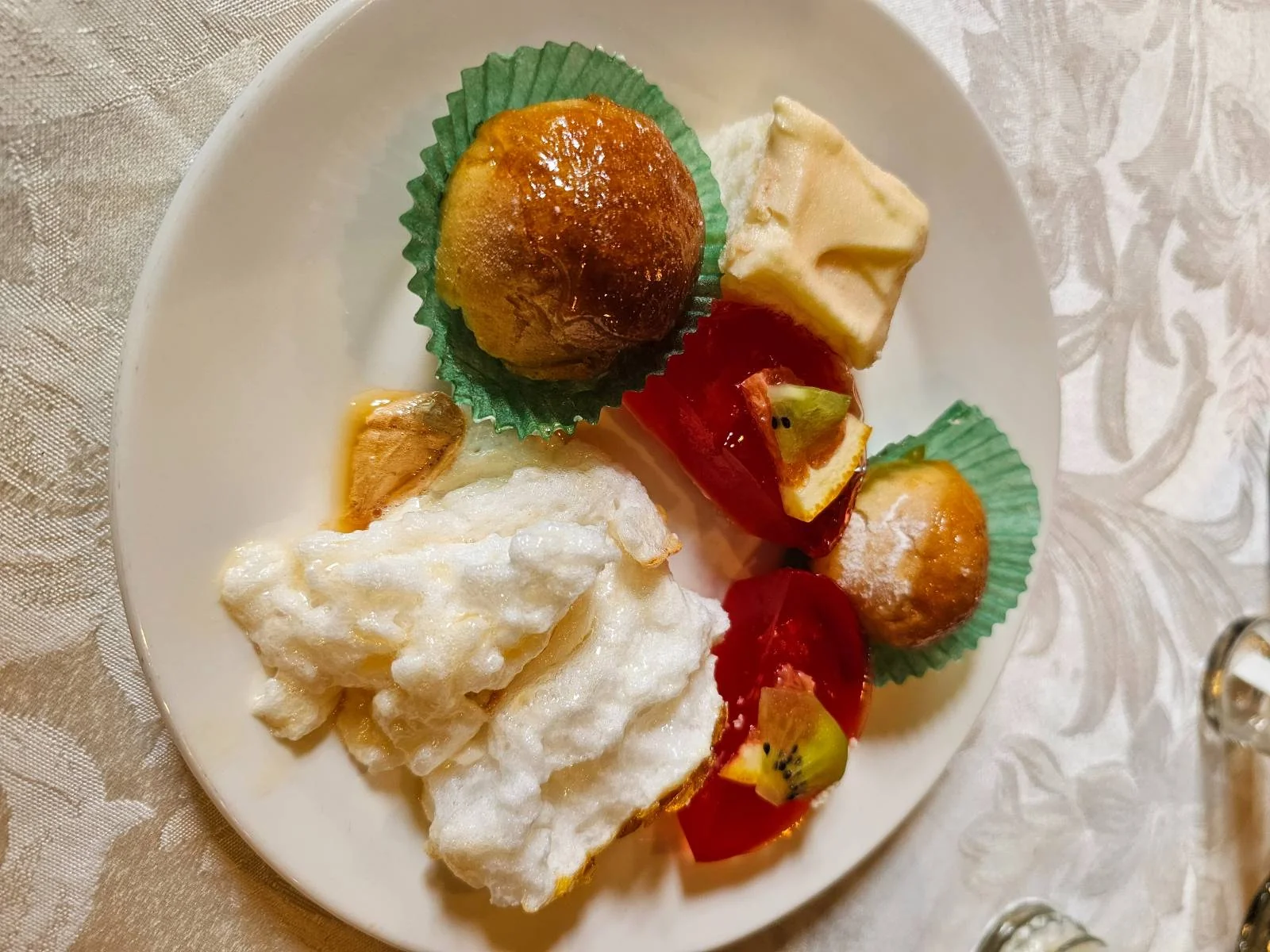 A dessert plate with pastries, a square of cake, whipped topping, and fruit jelly garnished with kiwi pieces.
