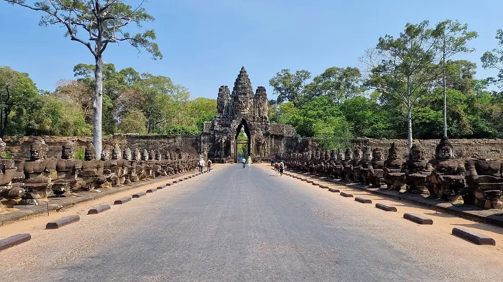 Ancient stone gate with statues on each side, trees in background. People walk along the pathway, sky is clear blue. Calm, historical scene.