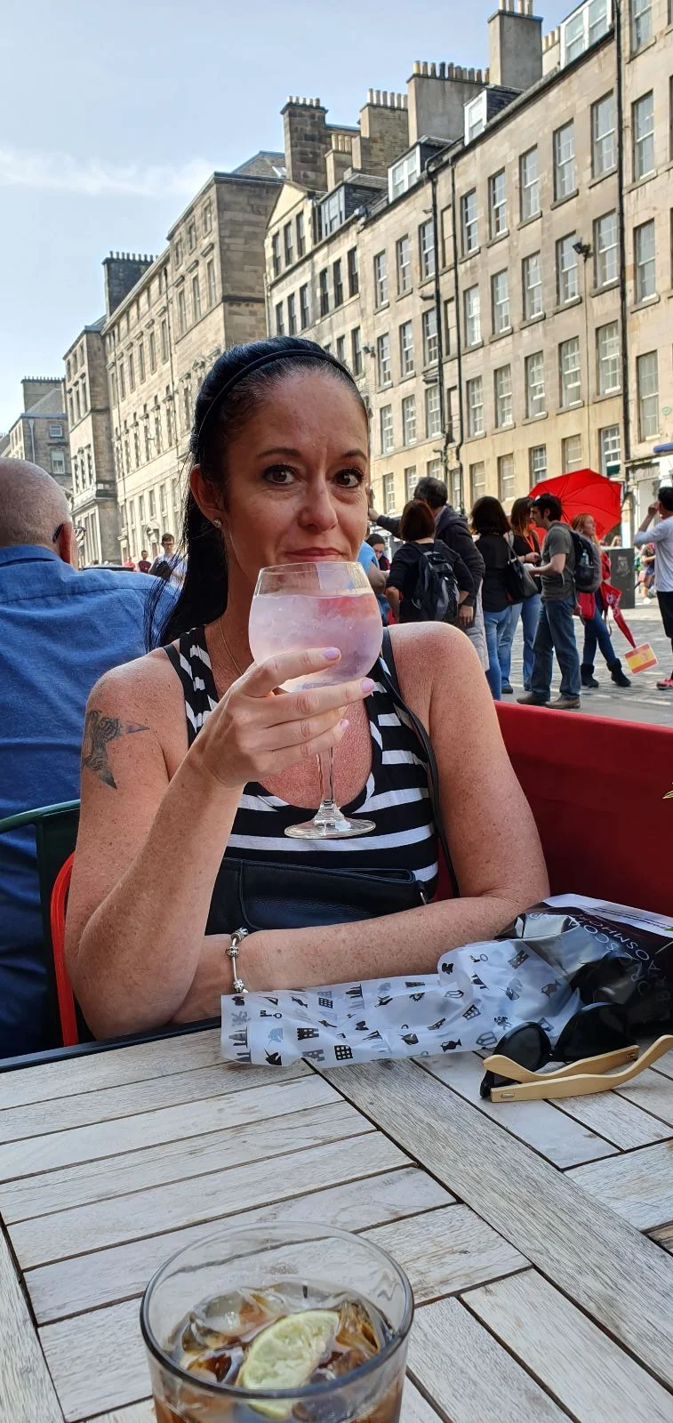 Jenn holding a gin and tonic at an outdoor café on the Royal Mile, with historic Edinburgh buildings and crowds behind.