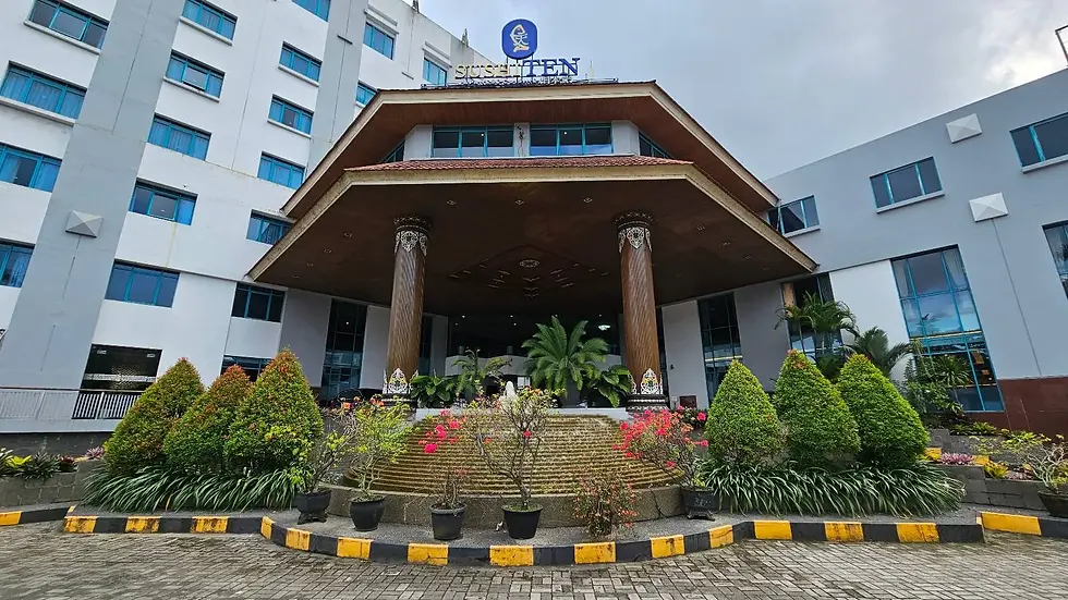 Entrance of a modern building with a tiled roof, large columns, and landscaped greenery. Overcast sky. Sign reads "SUSHITEN."