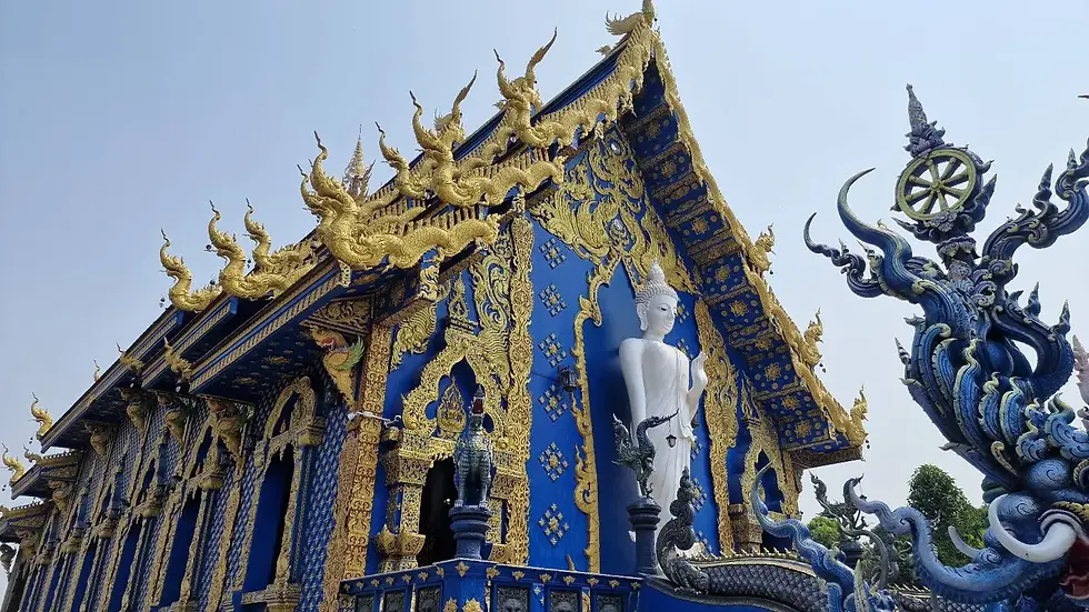 Blue temple with ornate gold details and a large white Buddha statue at the entrance, under a clear sky.