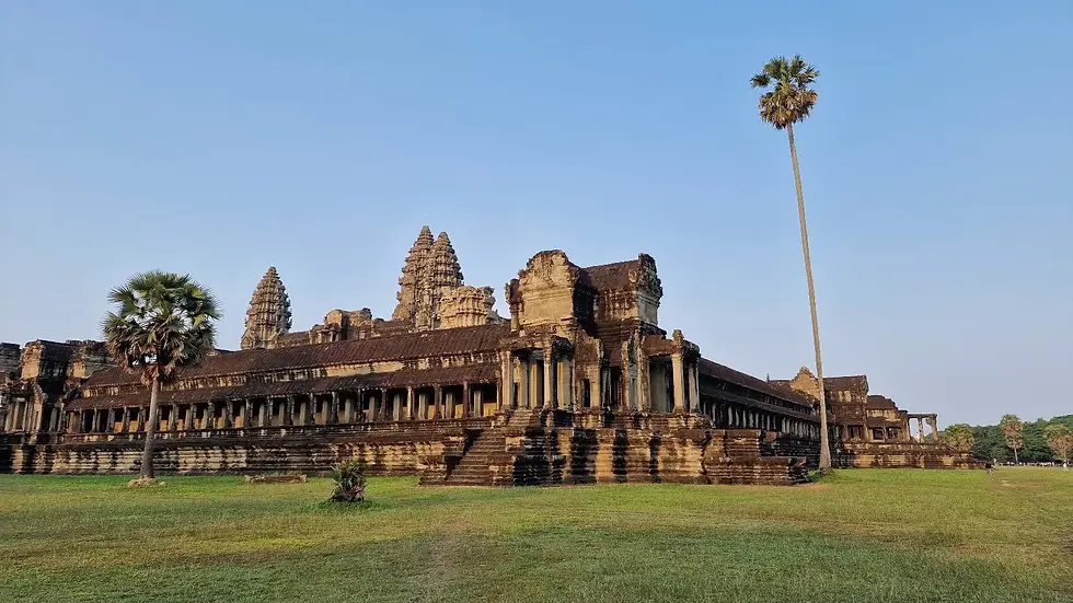 Ancient stone temple with intricate spires under a clear blue sky, surrounded by grass and tall palm trees, evoking a serene atmosphere.