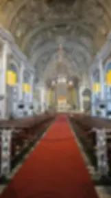 Ornate cathedral interior with arched ceiling, chandeliers, and red carpet leading to altar. Yellow banners hang on white columns. Quiet ambiance.