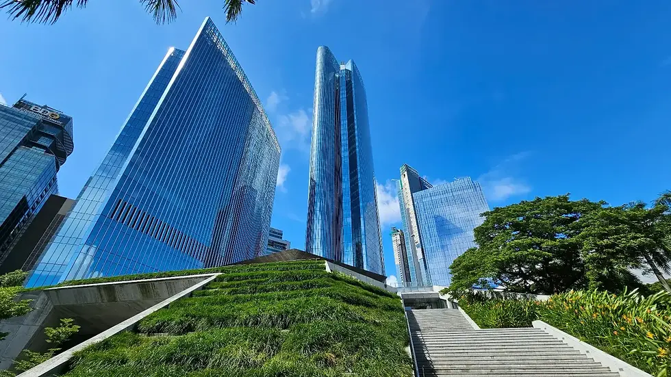 Skyscrapers against a blue sky, with a lush green hill and staircase in the foreground. Palm trees add a tropical vibe.