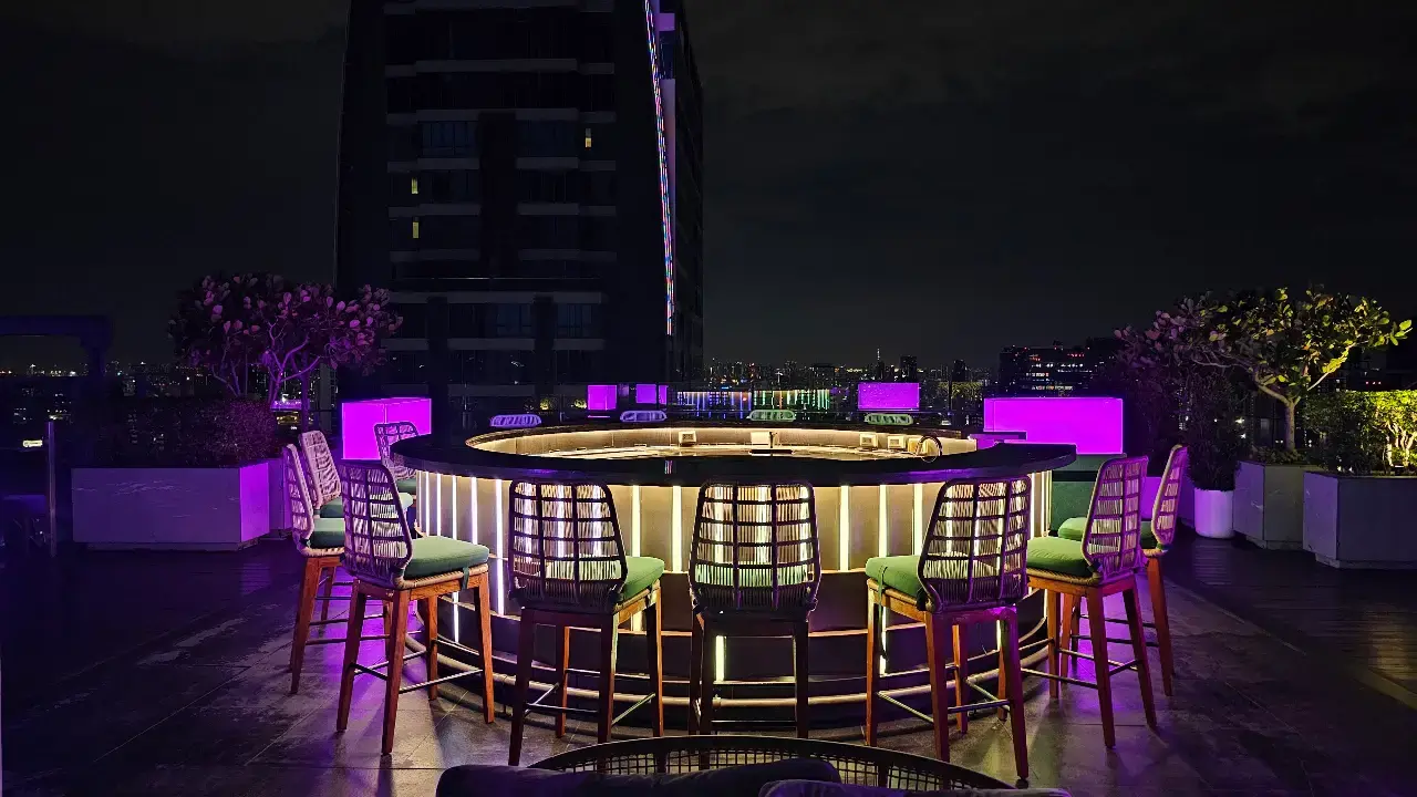 Purple-lit rooftop bar with high stools and panoramic city views.