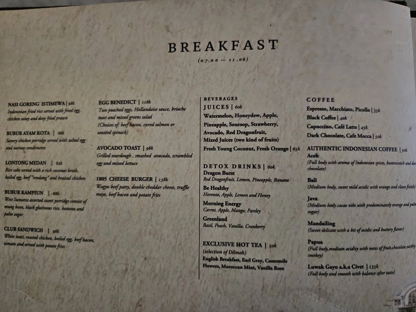 A breakfast menu with multiple sections listing various food and beverage options including pastries, sides, house specialties, coffee, cold brews, and extras. The text is printed on a textured, off-white background.