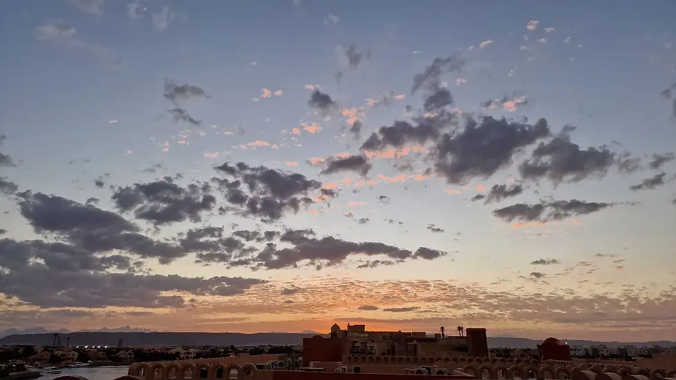 A sunset sky with scattered clouds over a cityscape featuring buildings and distant mountains.