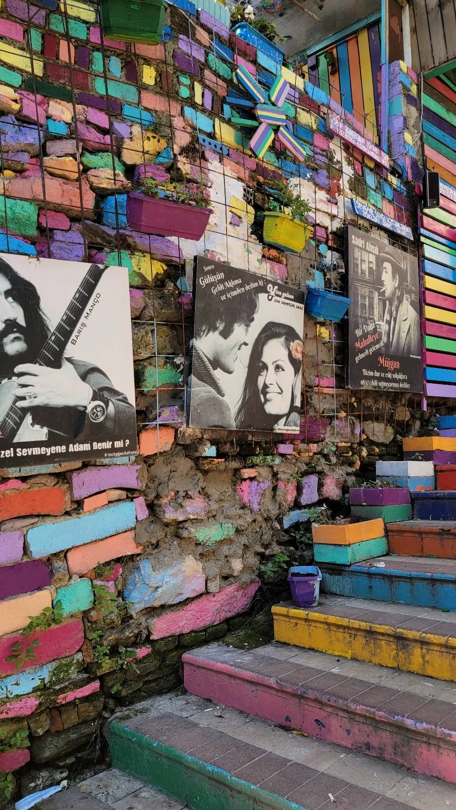 Colorful stairs with murals on a brick wall, displaying portraits of three individuals.