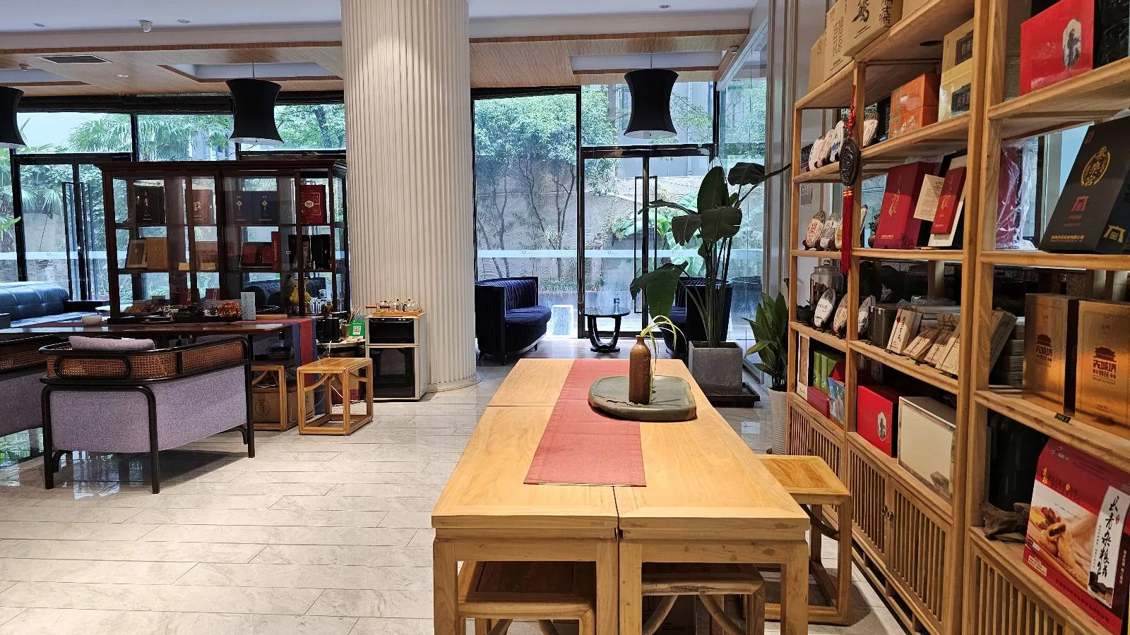 A modern library or reading room with wooden tables and chairs, bookshelves filled with colorful books, large windows letting in natural light, and potted plants enhancing the cozy atmosphere.