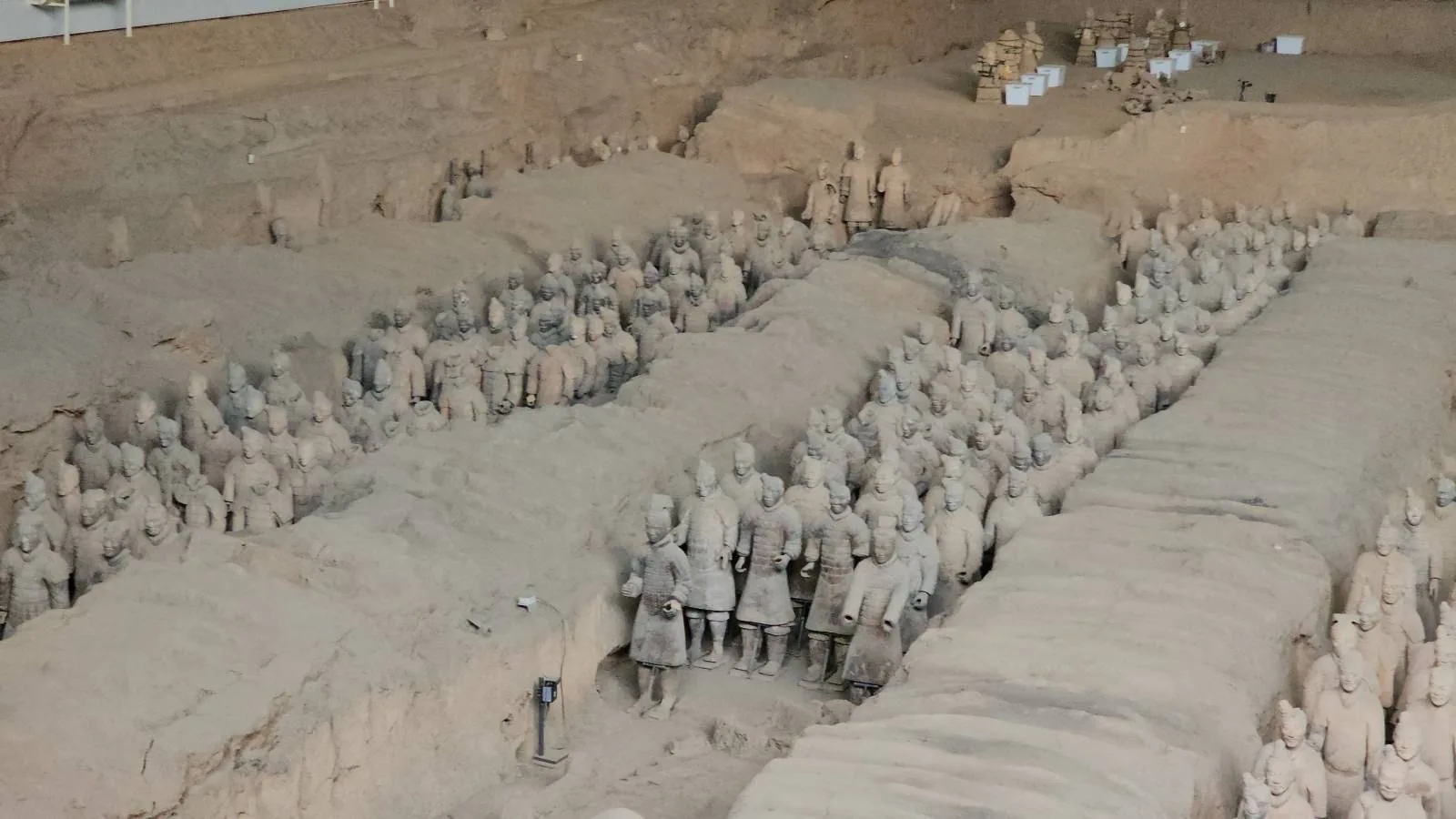Rows of terracotta warriors stand in excavated pits at the archaeological site of the Terracotta Army in Xi’an, China, with some life-sized statues partially buried and others fully uncovered.