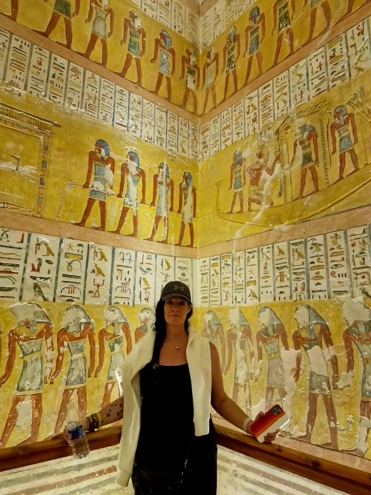 A person stands inside an ancient Egyptian structure, surrounded by walls covered in hieroglyphs and colorful, detailed paintings of figures.