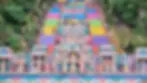 Colorful temple steps with vibrant statues and many people climbing. Lush greenery surrounds, creating a lively, spiritual scene.