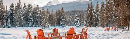 Red Adirondack chairs surrounding an outdoor snow-covered fire pit area at Baker Creek by Basecamp in Lake Louise, Canada.