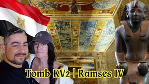 Man and woman smiling with Egyptian flag atop ancient tomb art. Black statue on the right. Text: "Tomb KV2 | Ramses IV."