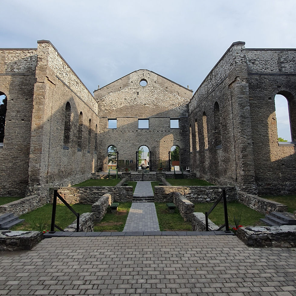Stone ruins of an old cathedral with arched windows. Sunlight casts shadows on the walkway leading through the open-air structure.