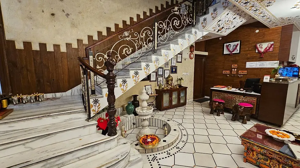 Ornate lobby with spiral staircase, white and gold floral design. Buddha statue, decorative furniture, marigold bowl. Warm, inviting mood.