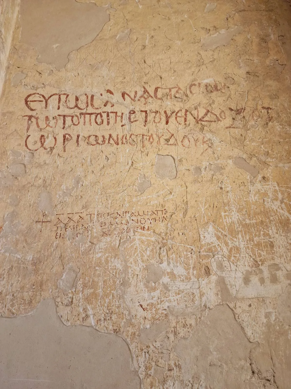 Ancient graffiti with Cyrillic inscriptions on a textured, aged wall. The text is in red and surrounded by worn plaster, suggesting historical significance and weathering over time.