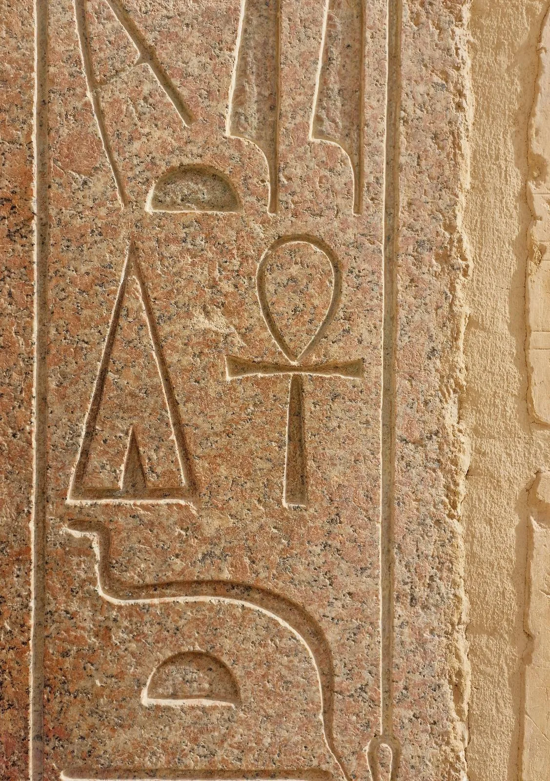 Close-up of ancient Egyptian hieroglyphs carved on a stone surface, featuring symbols including an ankh and a looped cross.