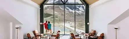 A cozy indoor lounge area with large viewing windows overlooking snowy mountains at Glacier View Lodge in Jasper, Canada.