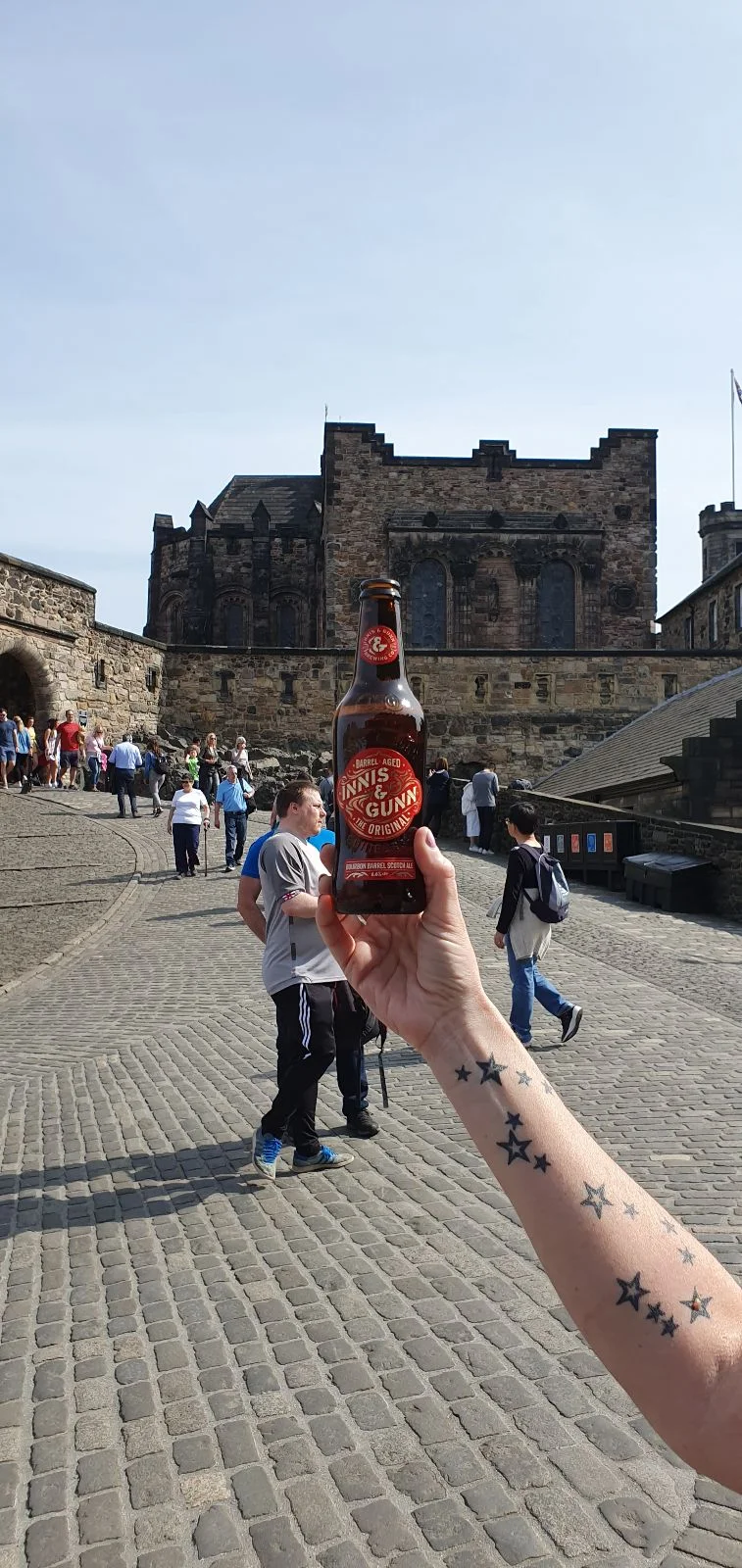 Jenn holding a beer up along the Royal Mile toward Edinburgh Castle, with visitors on the cobbled street.