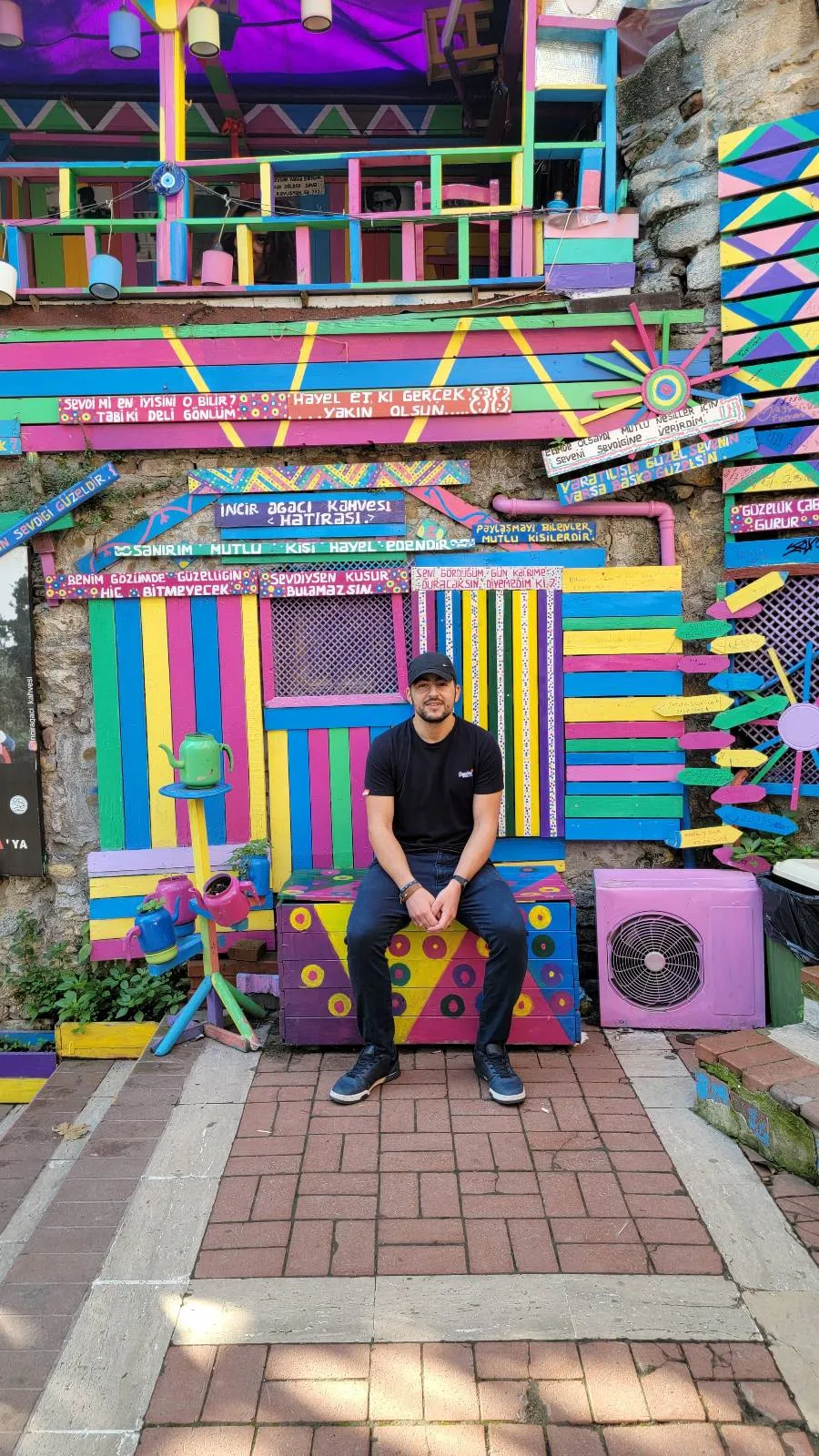 Person sitting in front of a colorful, abstract mural featuring geometric patterns and vibrant stripes.