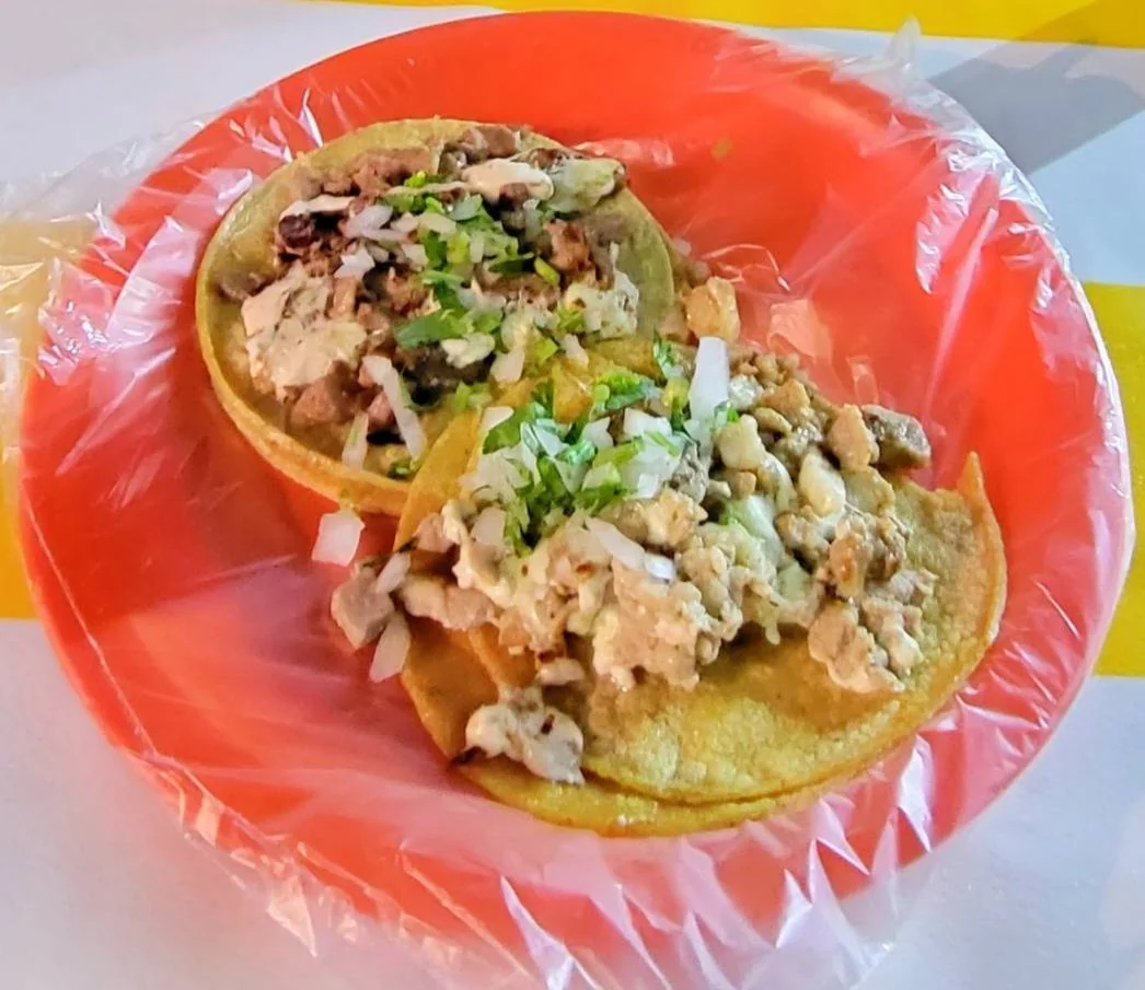 Two tacos on a red plate, each filled with chopped grilled meat, onions, and cilantro. The plate is lined with a plastic bag and set on a yellow and white table.