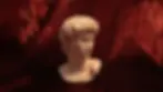 Bust of a classical sculpture on rich red velvet fabric background. The marble is white, detailed, and contrasts with the lush fabric.