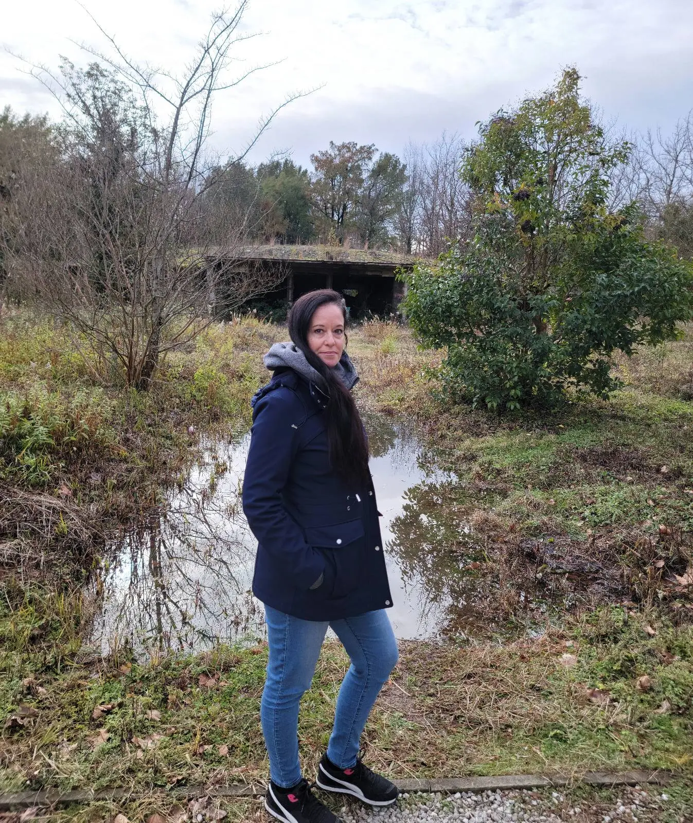 Woman standing on a trail with a water-logged field and a bridge in the background.