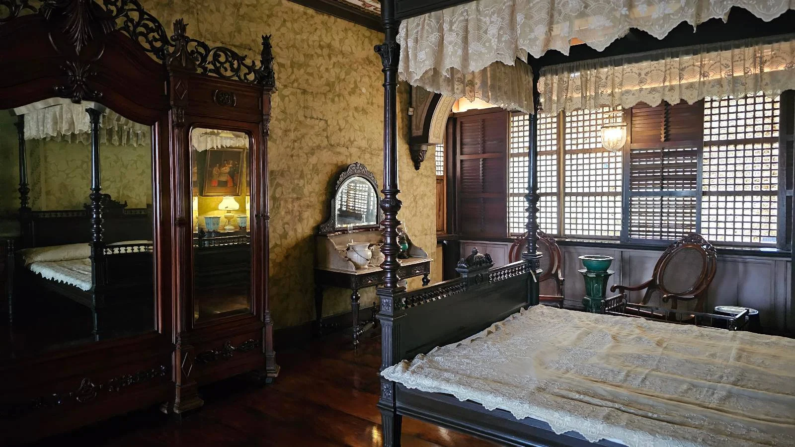 A vintage bedroom with a wooden four-poster bed, ornate wardrobe with mirrored doors, and an antique vanity. Warm lighting and lace curtains create a nostalgic and cozy atmosphere.