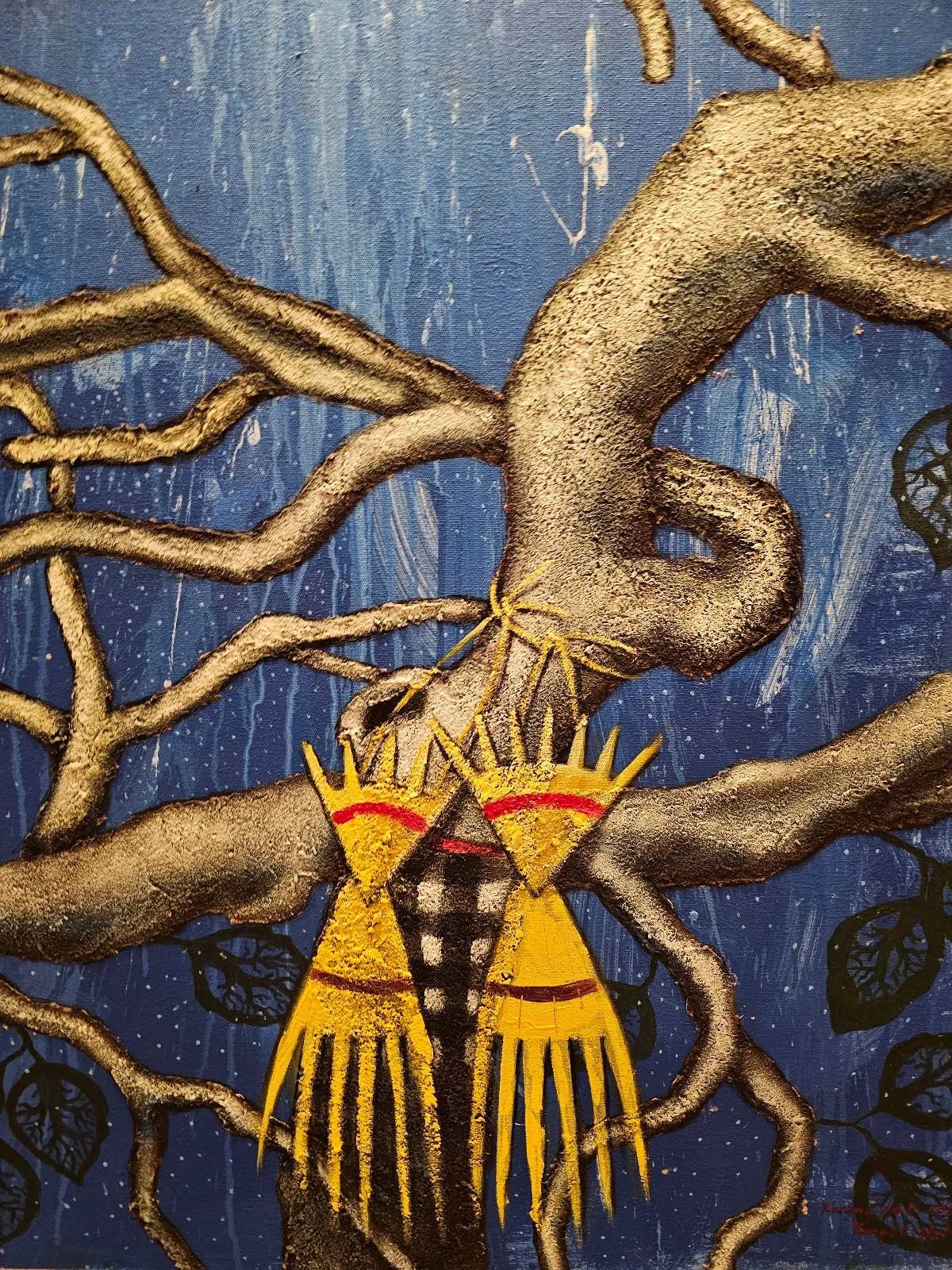 Two yellow, red, and orange Native American-style decorative objects hang from the branches of a twisting tree against a blue background with faint hints of foliage.