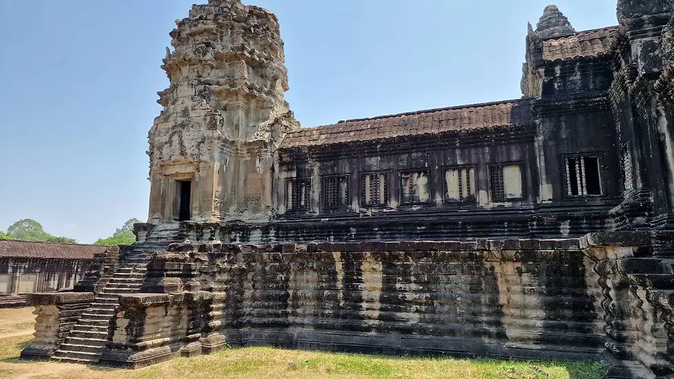 Ancient stone temple with intricate carvings and steps in a sunny outdoor setting. Weathered gray and beige tones against a clear blue sky.