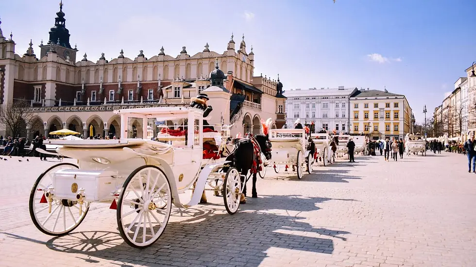 White horse-drawn carriages line cobblestone square; people walk nearby. Historic building with ornate facade under a clear blue sky.