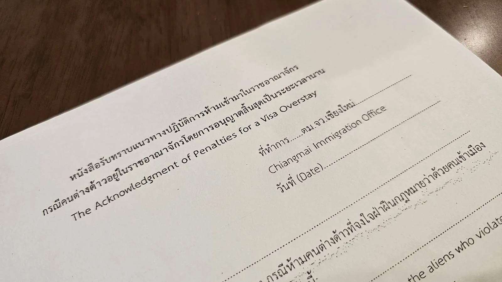 A close-up of a document titled "Acknowledgement of Intention for a Visa On-arrival" written in Thai and English, with blank spaces for name, passport number, and arrival date information. The paper is resting on a dark wooden surface.