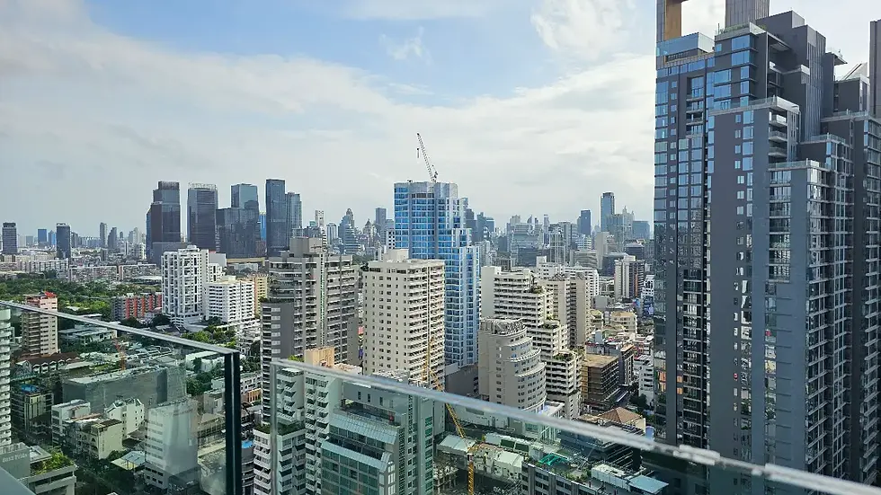 High-rise city skyline viewed from a balcony, with glass railings, dense towers, and a bright cloudy sky.