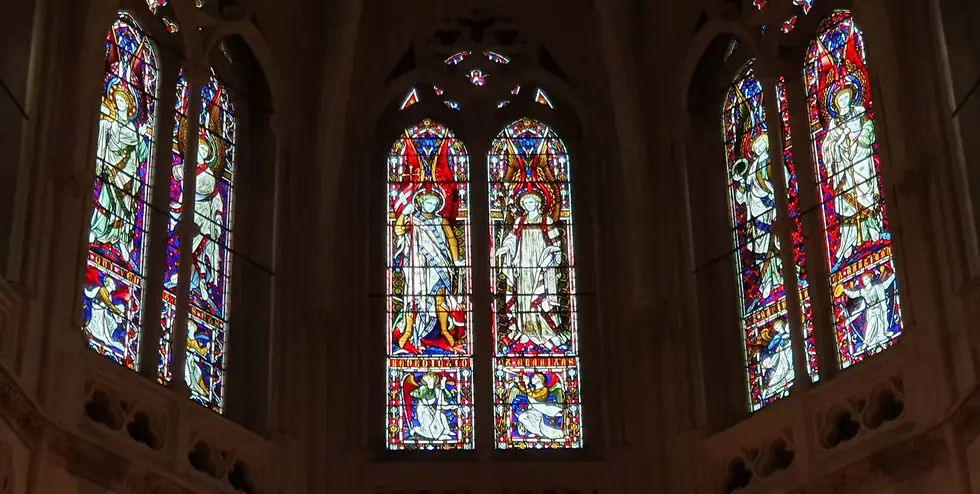 Stained glass windows in a cathedral depict angels with vibrant colors. Gothic architecture surrounds, creating a serene, spiritual ambiance.