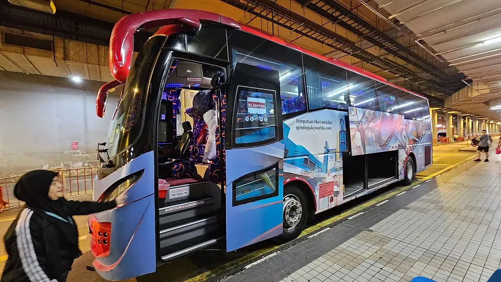 A colorful bus with open doors in a terminal. A person in a hijab boards. "KL Sentral" visible. Vibrant seat patterns inside.