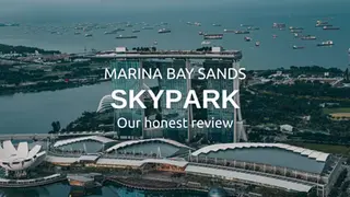 Aerial view of Marina Bay Sands SkyPark with text: "MARINA BAY SANDS SKYPARK Our honest review." Ocean and ships in the background.