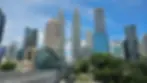 Futuristic bridge with spiral design leads to skyline, including twin towers, under bright blue sky. Two people walking on the bridge.