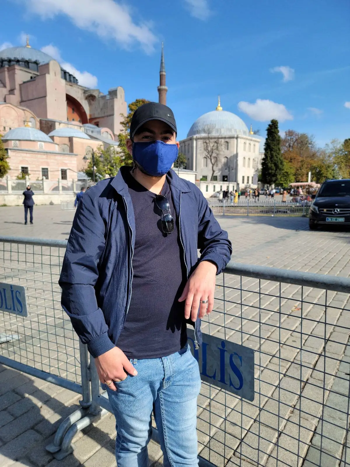 Person in a blue mask and jacket standing in front of a historic building on a sunny day.
