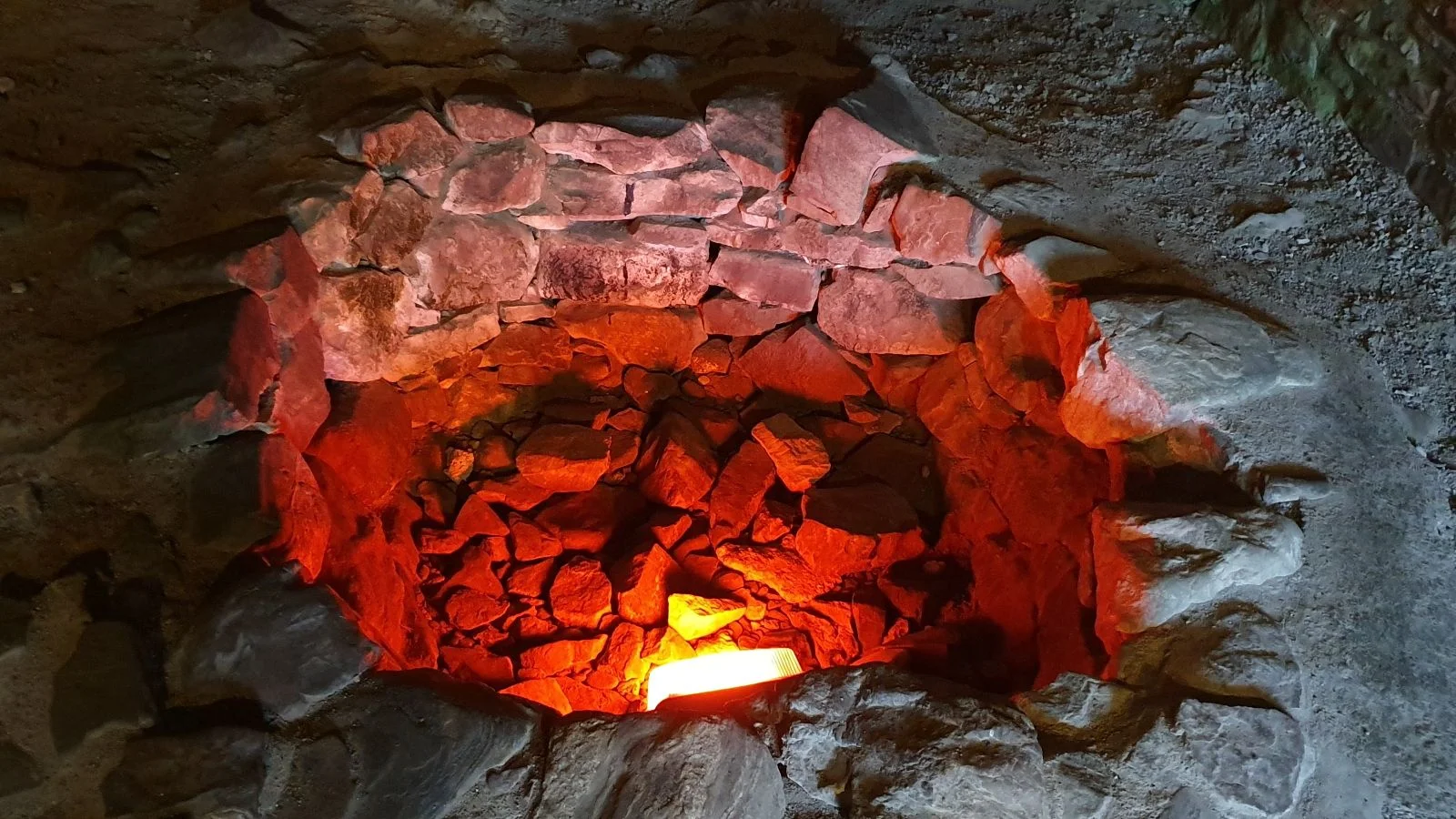 Stone-lined furnace or hearth inside Urquhart Castle with glowing embers and firelight.